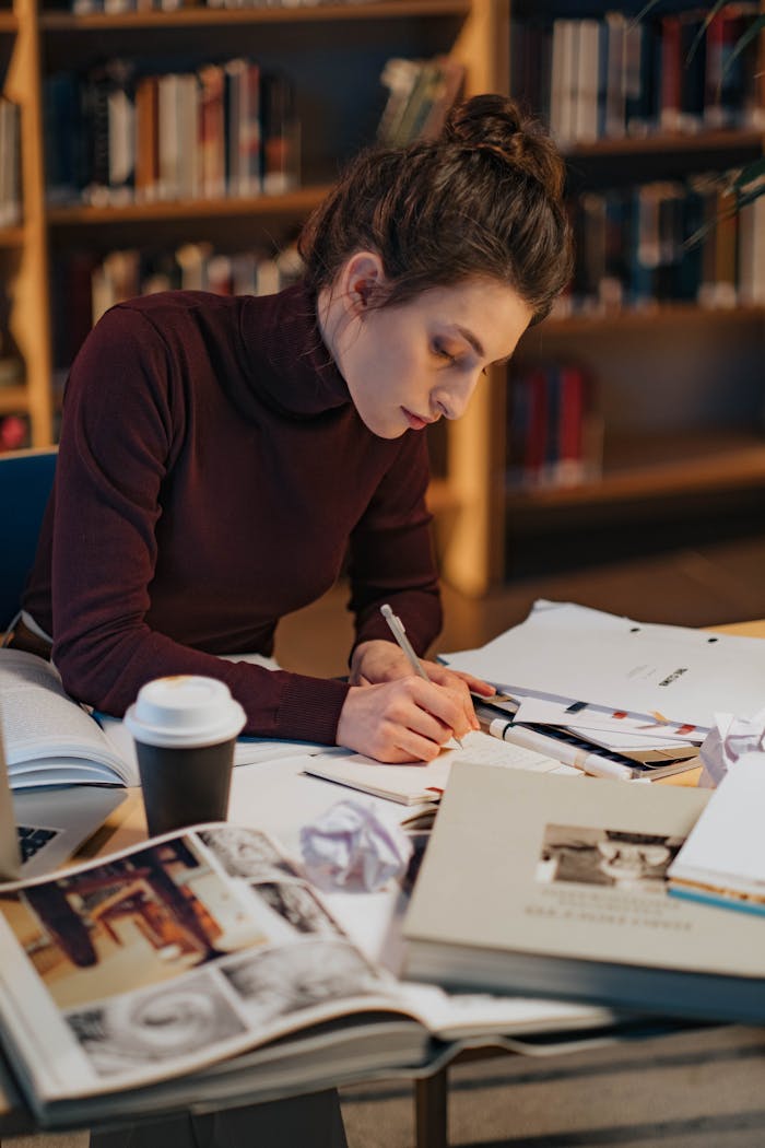 Young woman deeply engaged in writing, surrounded by books in a cozy library setting.